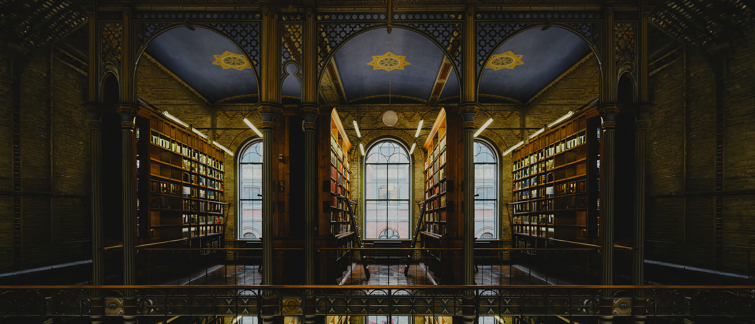 Long, dimly lit library with bookshelves on either side and large windows at the end.